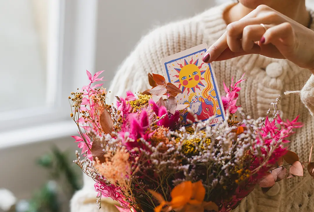 Main de Marjorie sortant une carte de tarot d’un bouquet de fleurs