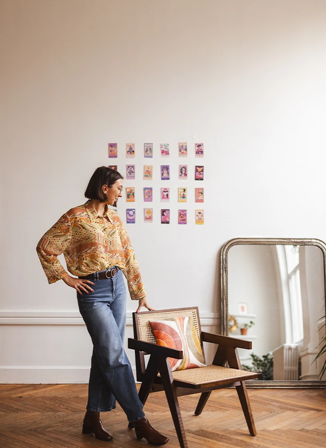 Marjorie debout appuyée sur une chaise rétro, illustrant sa posture de coach tarot