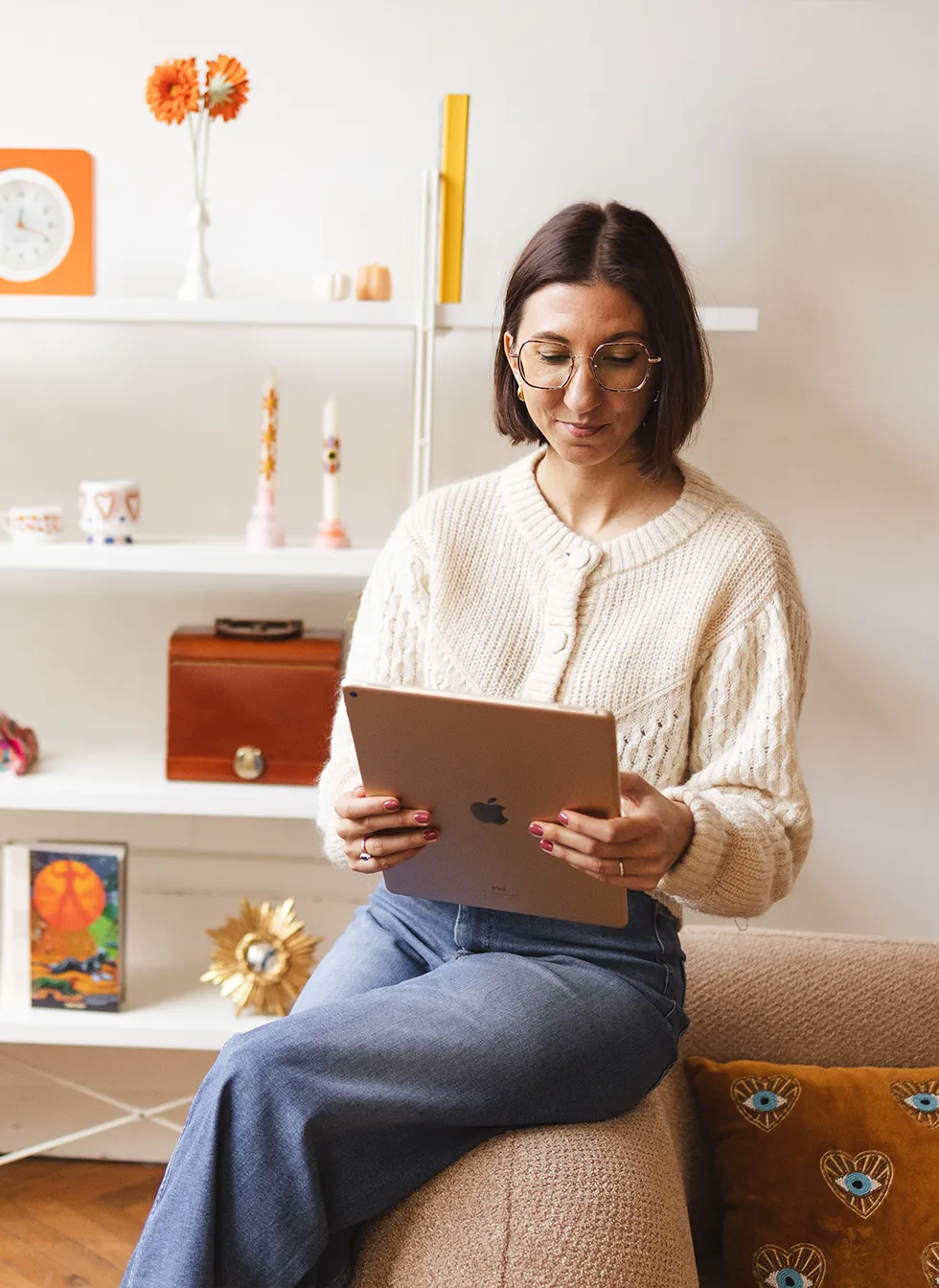 Marjorie consultant l'ebook tarot sur une tablette assise sur un canapé